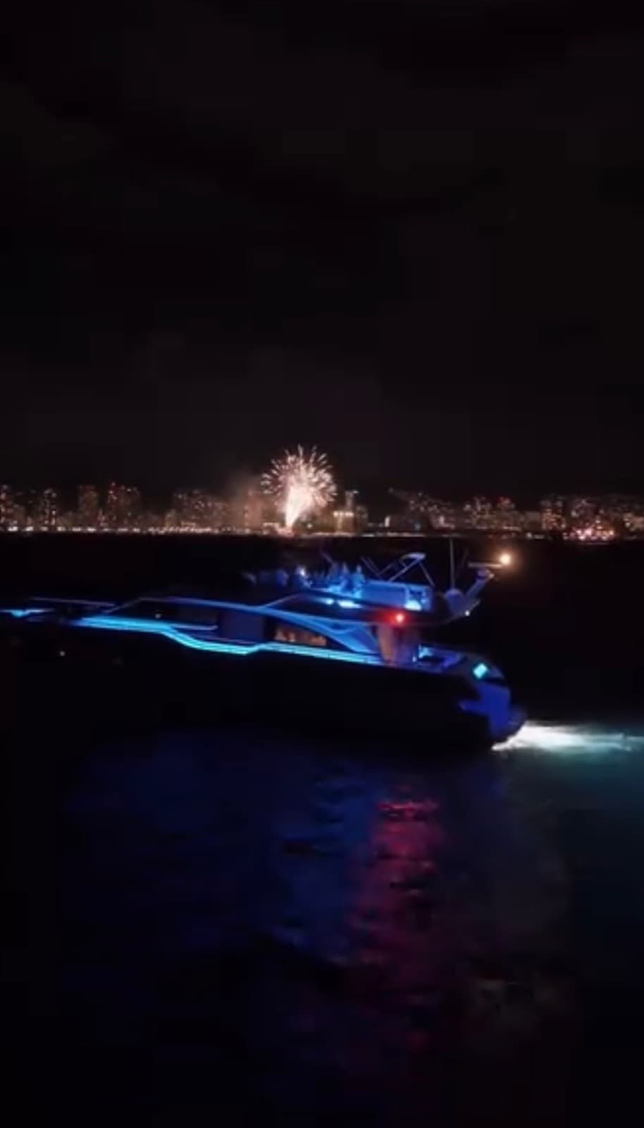 The Alana Kai lit in blue underwater lighting at night, fireworks over the city.