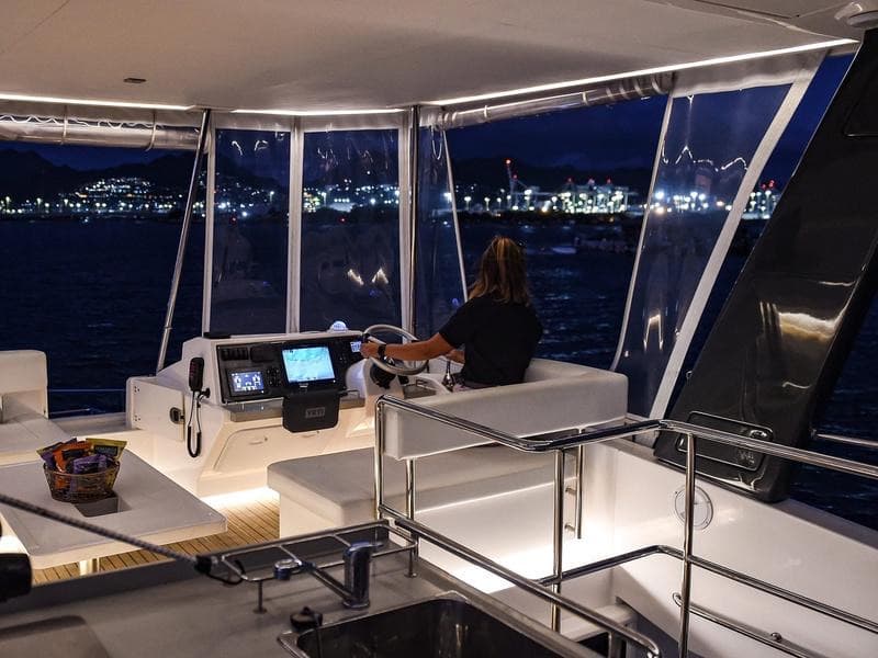 The captain at the lit flybridge helm with harbor lights behind.